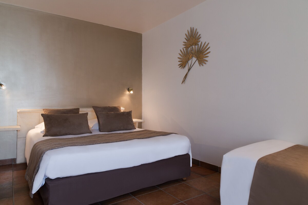 A neatly made bed with a white and brown bedspread, a bedside table with a lamp, and a wall-mounted decorative piece.