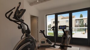 A home gym with exercise equipment, a large window with a view of a house and a swimming pool, and a door leading to another room. - Val Baussenc, The Originals Relais (Maussane-les-Alpilles)