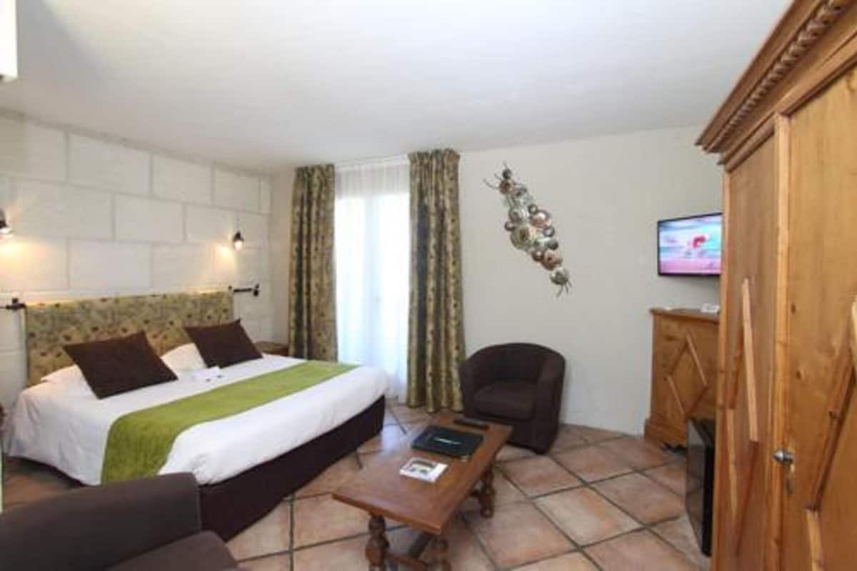 A hotel room with a bed, a chair, a wooden cabinet, and a television on the wall.