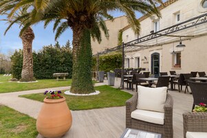 Un espacio al aire libre con mobiliario de mimbre, una jardinera grande con flores y una palmera.