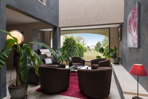 Una sala de estar moderna con sofás marrones, una mesa de centro de vidrio y plantas en macetas.