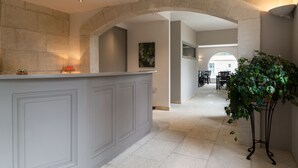 A reception area with a stone archway, a reception desk, a potted plant, and a dining area with tables and chairs in the background. - Val Baussenc, The Originals Relais (Maussane-les-Alpilles)