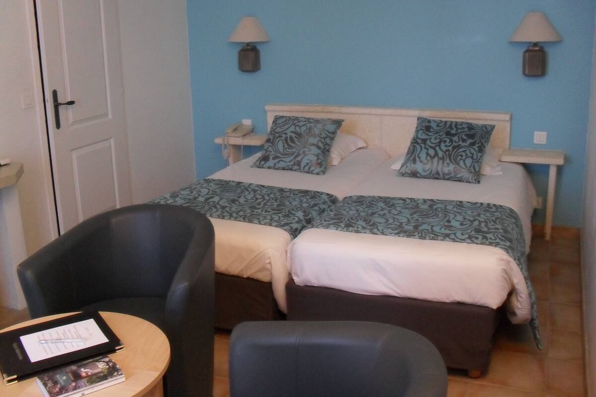 A hotel room with a bed, two bedside lamps, a chair, and a small table with a book.