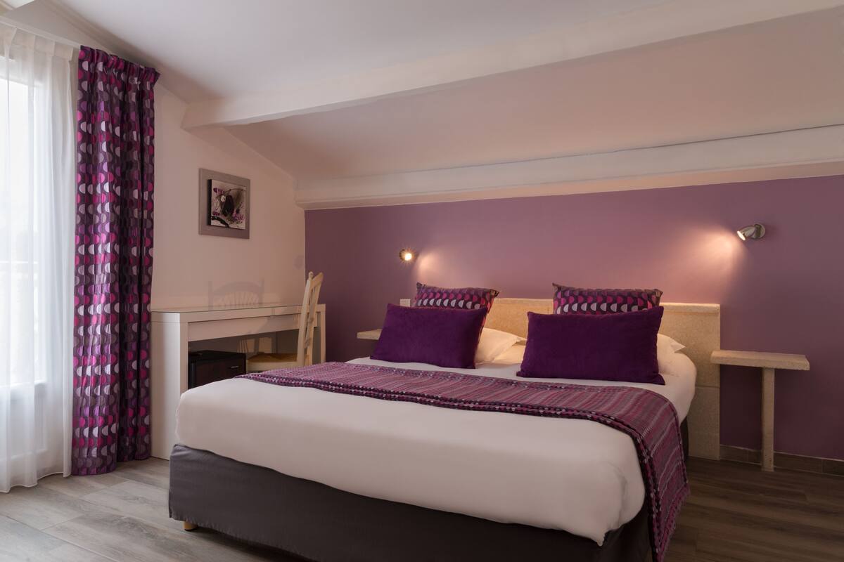 A bedroom with a bed, purple walls, and a desk.