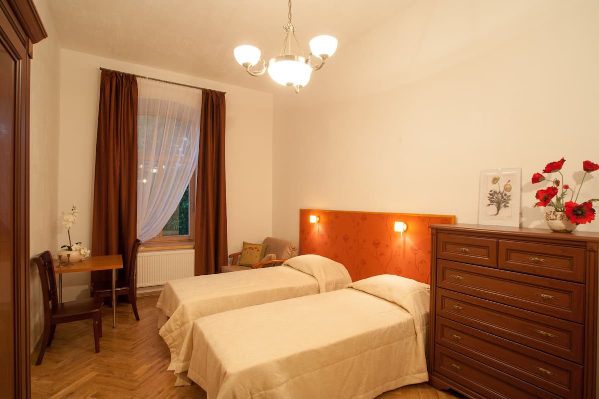 A hotel room with two beds, a wooden dresser, a desk with a chair, and a window with curtains.