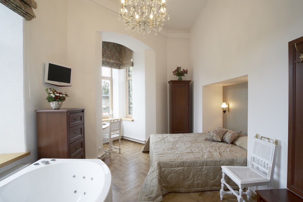 A bedroom with a large bed, a small table, a chair, a TV, a cabinet, and a window.