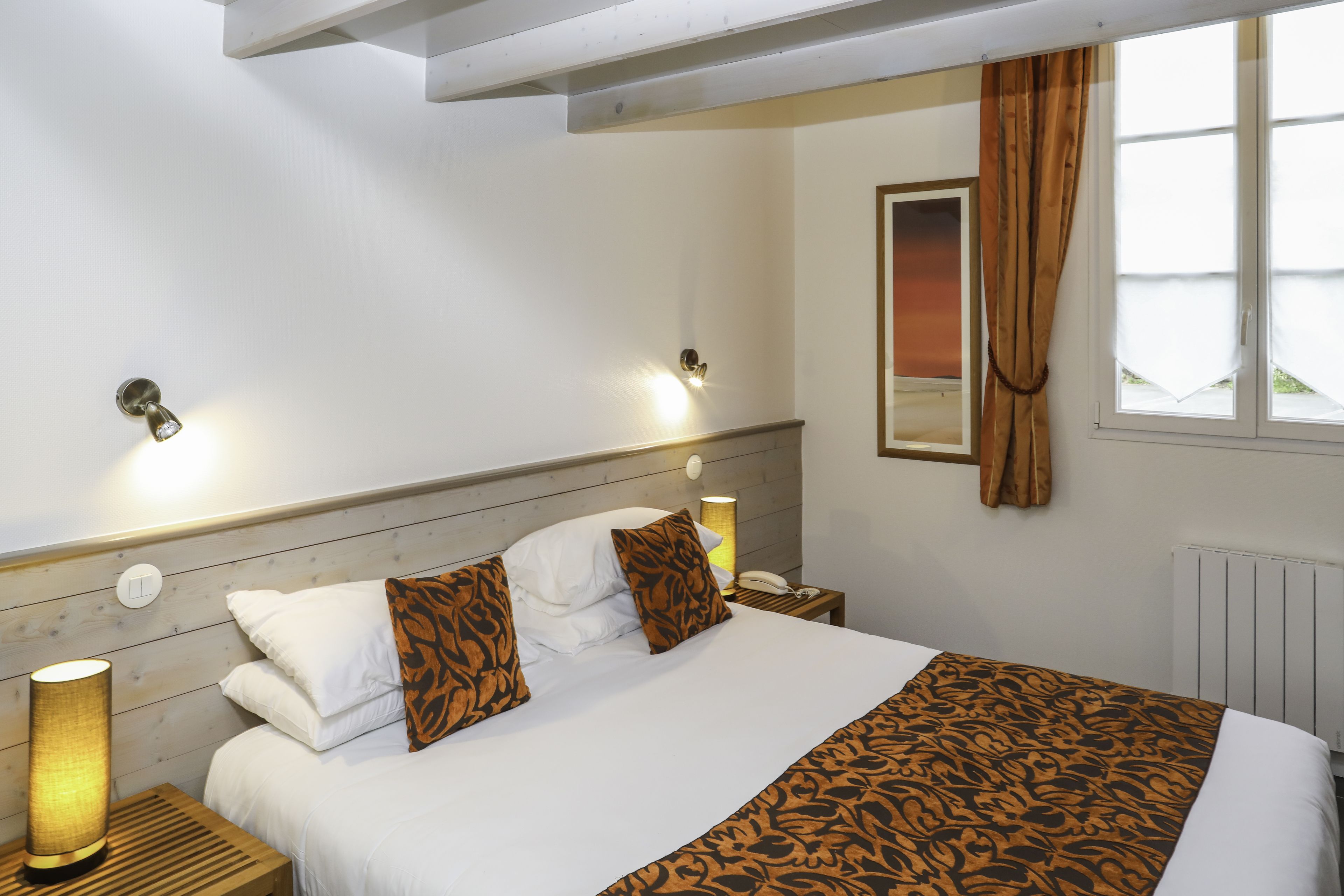 A neatly made bed with white linens and patterned pillows, a bedside lamp, and a nightstand with a phone.