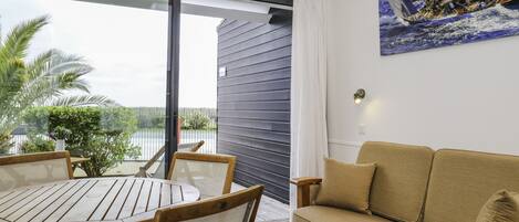 Una habitación moderna con una mesa y sillas de madera, un sofá, un ventanal con vistas a palmeras y un balcón.