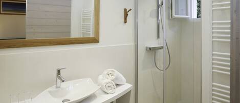 Un baño moderno con lavamanos, espejo y ducha blancos.