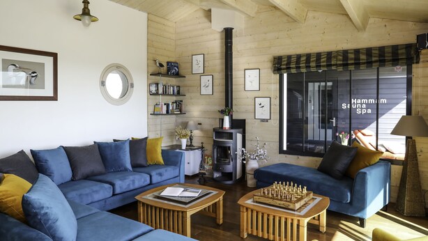 A cozy living room with blue sofas, a fireplace, and a view of Hammam Sauna Spa.
