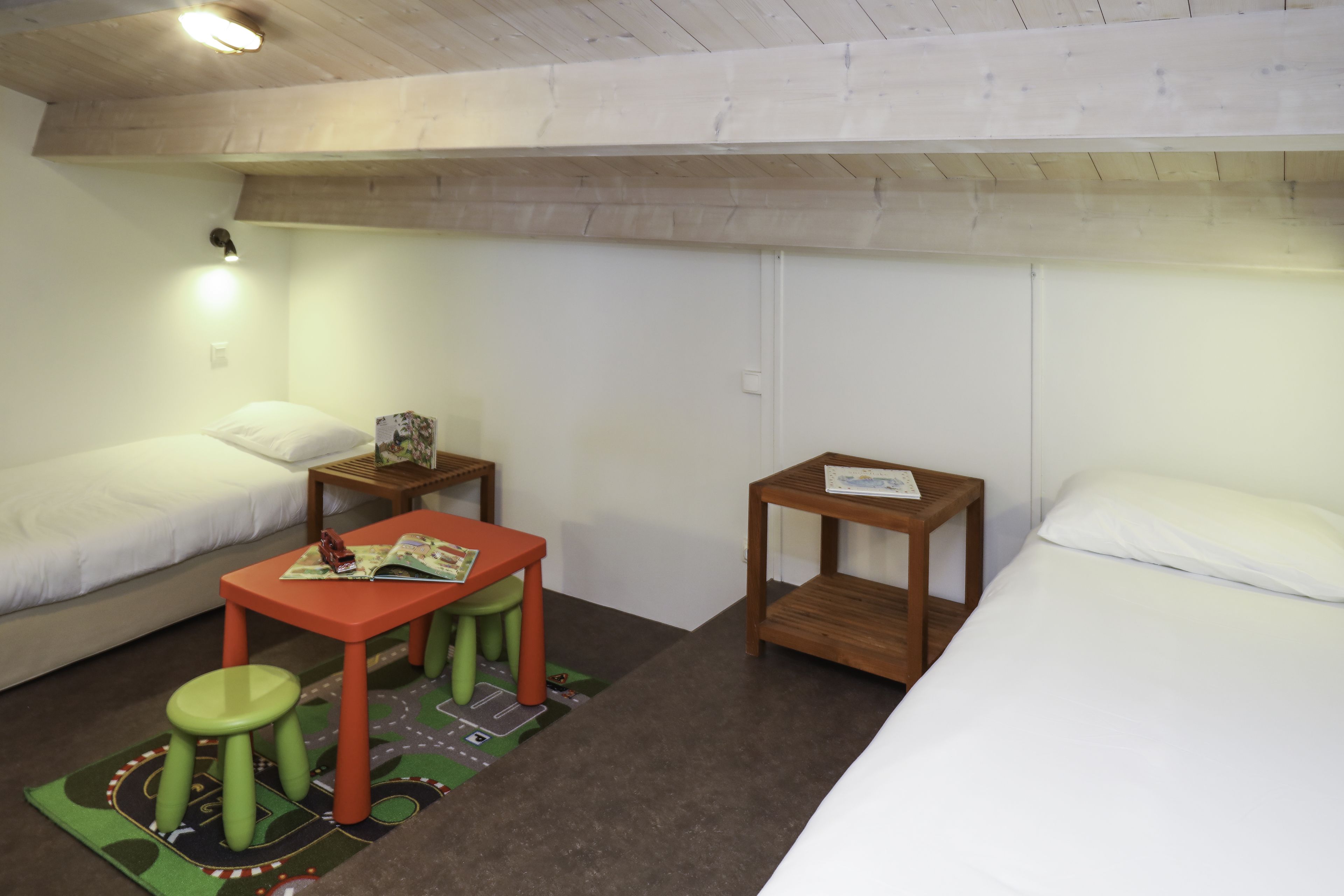 A room with two beds, a small table with stools, and a single nightstand.