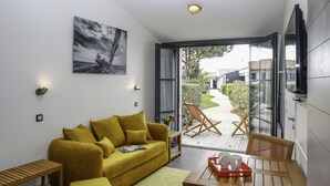 A modern living room with a yellow sofa, a wooden coffee table, and a glass door leading to an outdoor area with a garden and a wooden deck.