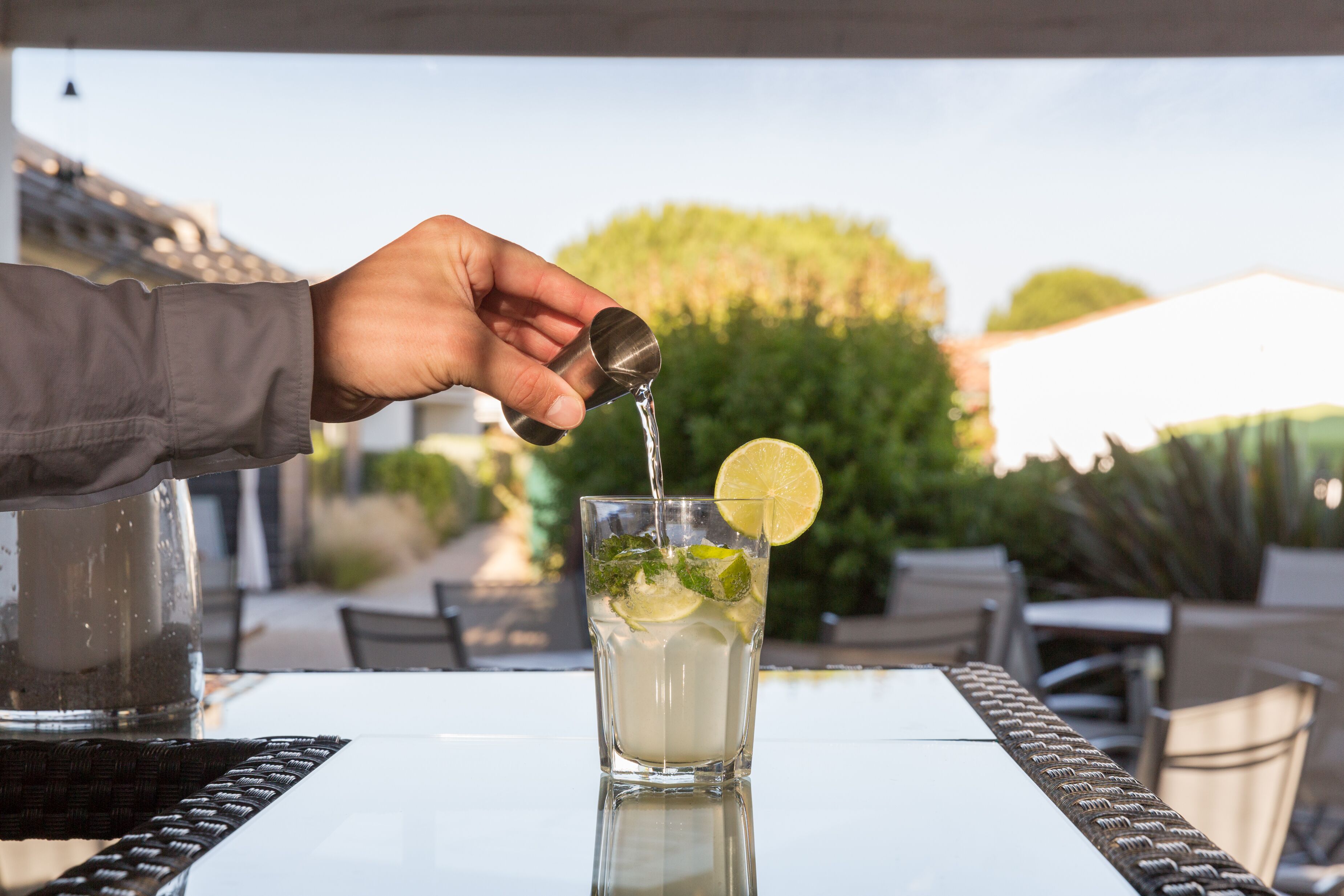 Une main verse une boisson dans un verre, dans lequel on a ajouté une tranche de citron vert et quelques feuilles de menthe.