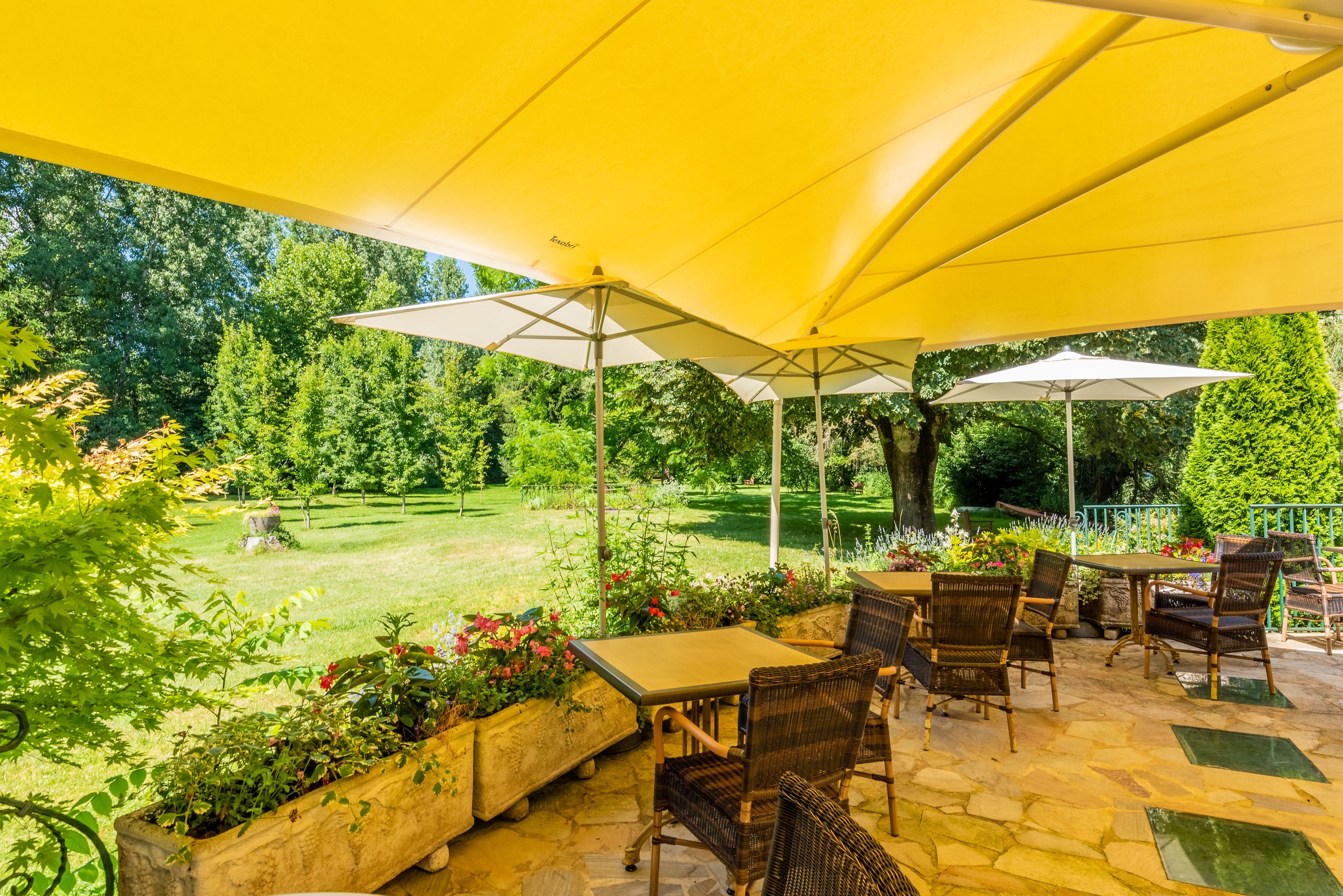 Une terrasse extérieure agrémentée de parasols jaunes, de meubles en osier et offrant une vue sur un jardin bien entretenu.