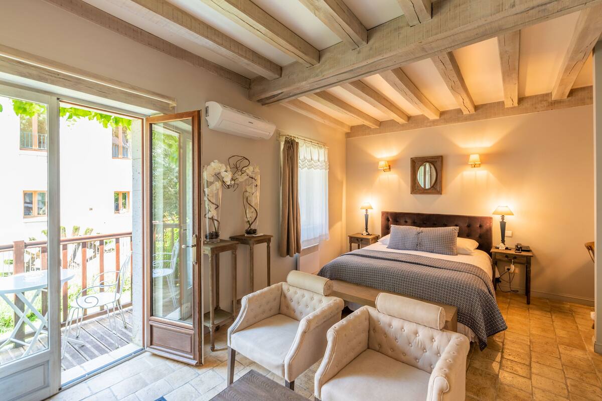 A bedroom with a large bed, two bedside tables, a nightstand, a sofa, and a sliding glass door leading to an outdoor area.
