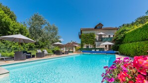 A swimming pool with lounge chairs and umbrellas, surrounded by greenery and a building with a stone facade. - Moulin de Vigonac (Brantôme en Périgord)