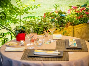 A table set outdoors with a potted plant, wine glasses, and cutlery.