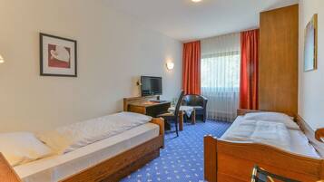 A hotel room with two single beds, a desk with a television, a chair, and a window with red curtains.
