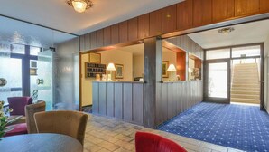 Un vestíbulo de hotel con una recepción, zona de estar y una escalera que lleva a otro piso.