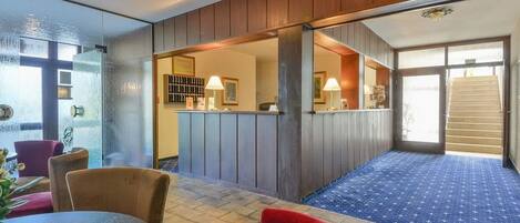 A hotel lobby with a reception desk, seating area, and a staircase leading to another floor.