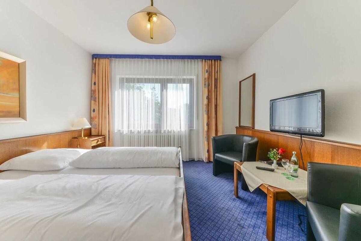 Habitación de hotel con dos camas, un escritorio con silla, televisor y ventana con cortinas.
