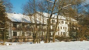 A multi-story building with a symmetrical facade, surrounded by snow-covered ground and leafless trees.