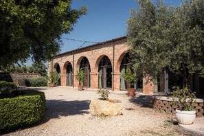 A courtyard with a brick building featuring arched doorways, surrounded by potted plants and a gravel path. - Villa Bongiovanni (San Bonifacio)