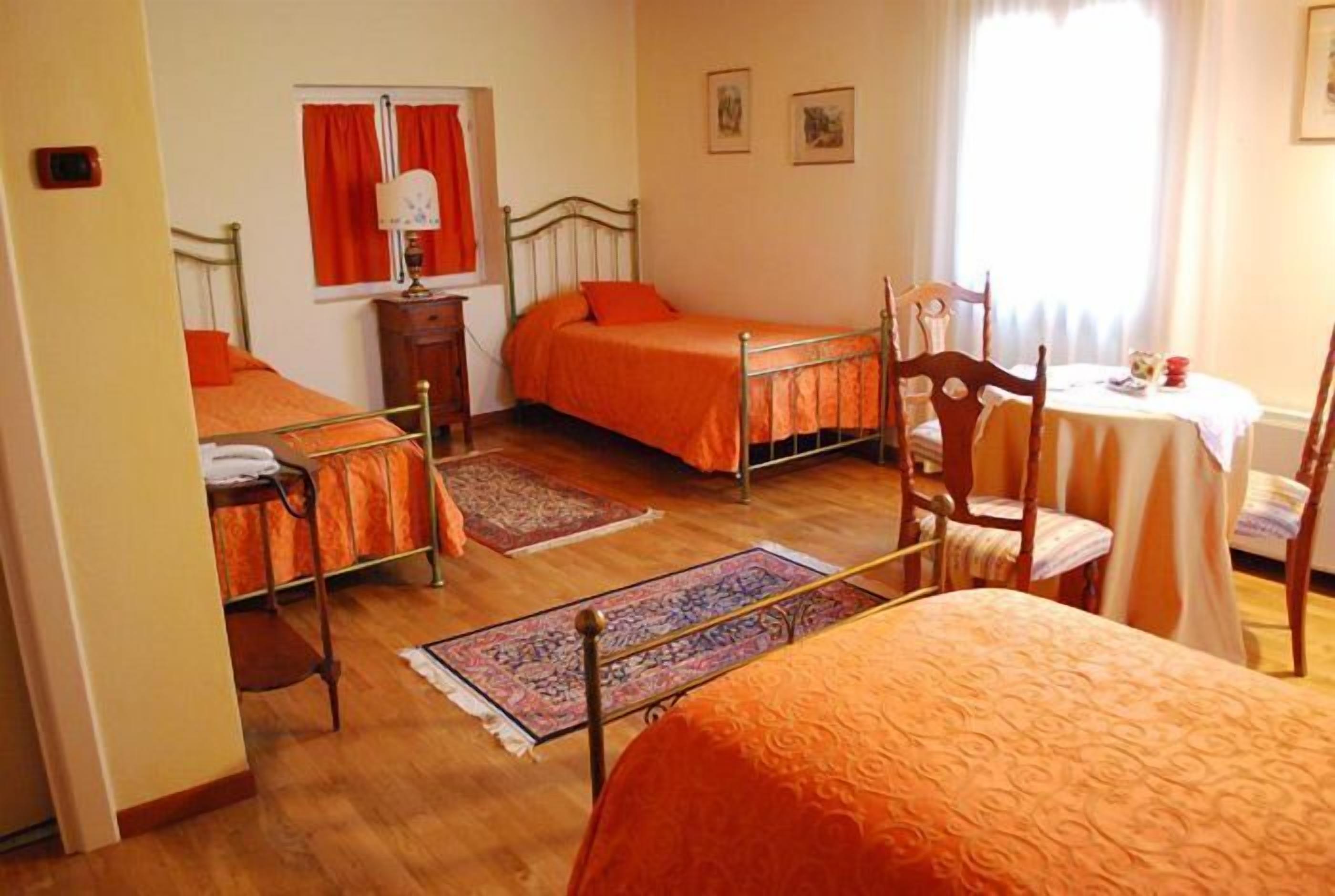 A room with two single beds, a wooden chair, a small table, and a window with curtains.