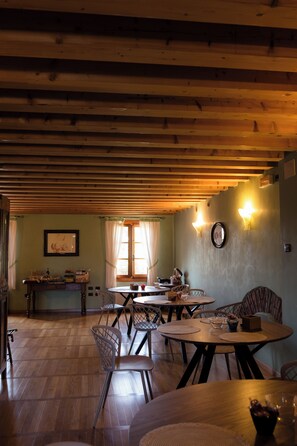 A dining area with wooden tables and chairs, a wooden ceiling, and a window with curtains. - Villa Bongiovanni (San Bonifacio)