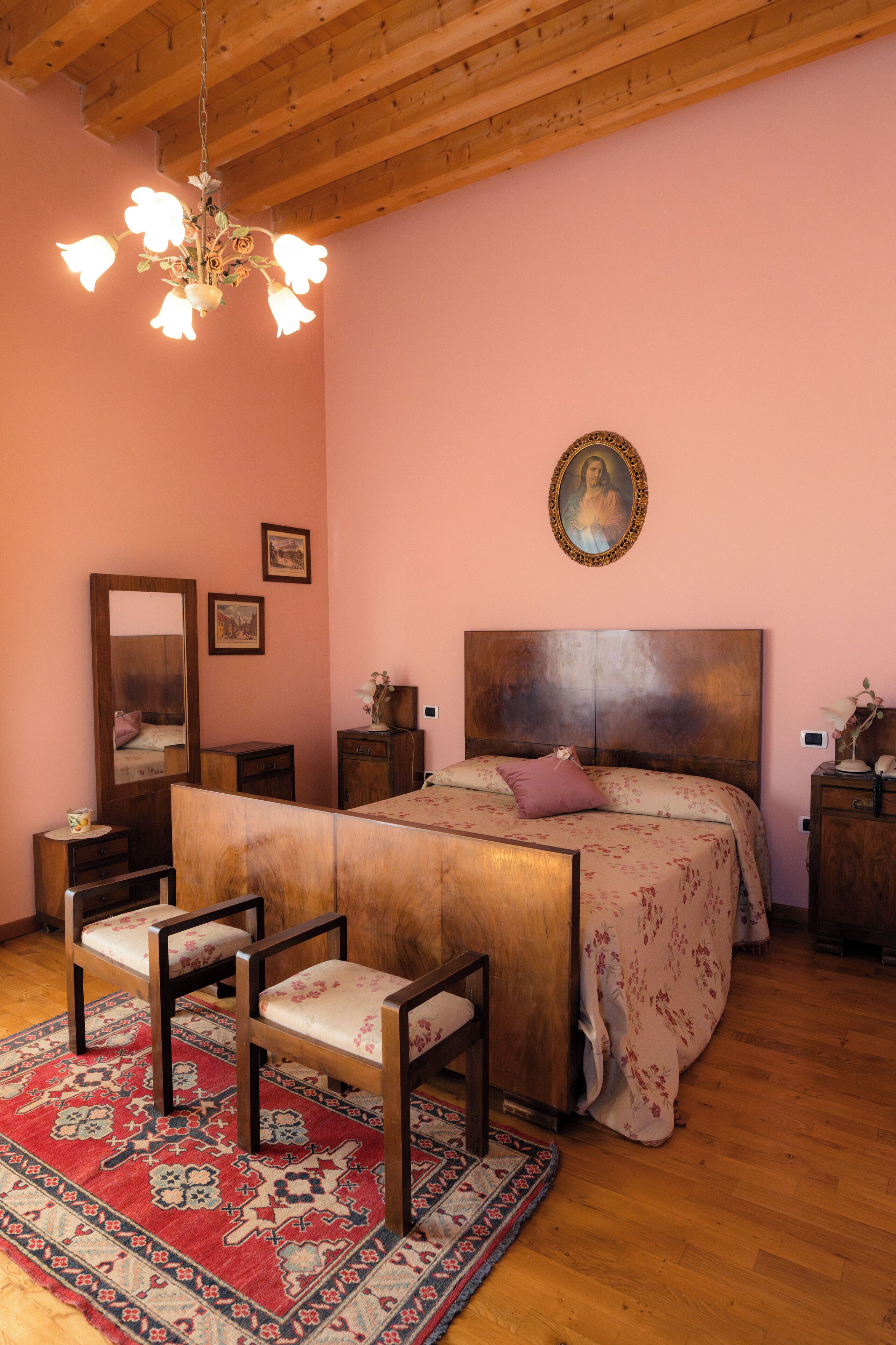 Un dormitorio con techo de madera, una cama con colcha floral, una mesita de noche de madera, una silla, un espejo y una araña.