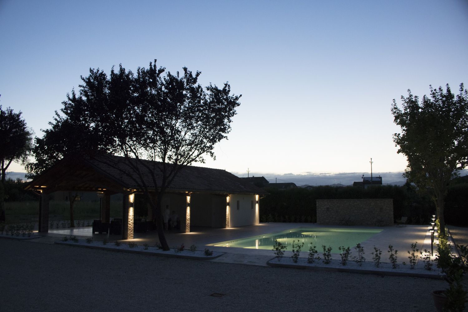 Uma área externa coberta com piscina, cercada por árvores e um muro de pedra.