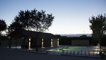 Uma área externa coberta com piscina, cercada por árvores e um muro de pedra.