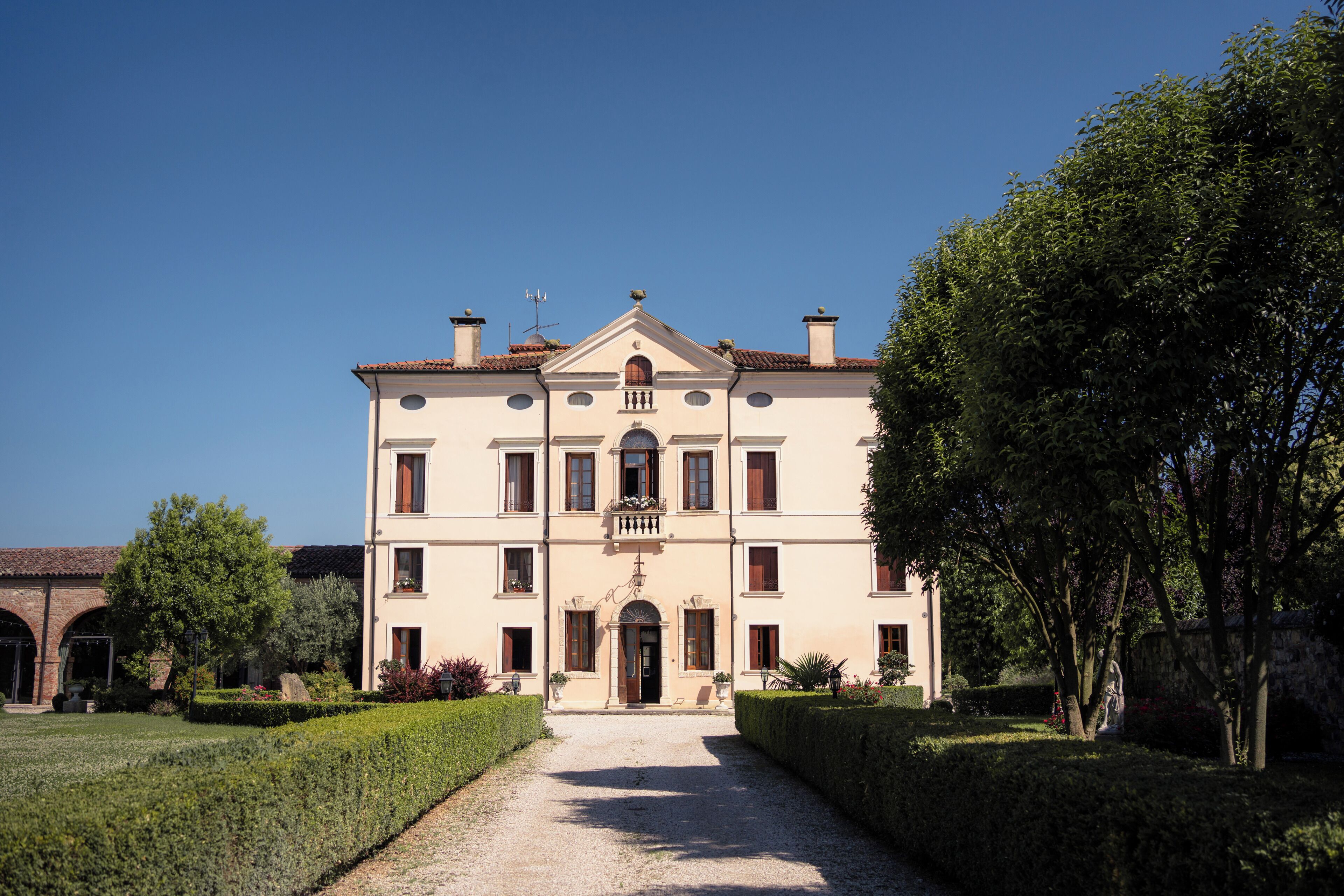 A large, symmetrical building with a central entrance, multiple windows, and a well-maintained garden with hedges and trees.