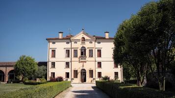 A large, symmetrical building with a central entrance, multiple windows, and a well-maintained garden with hedges and trees.