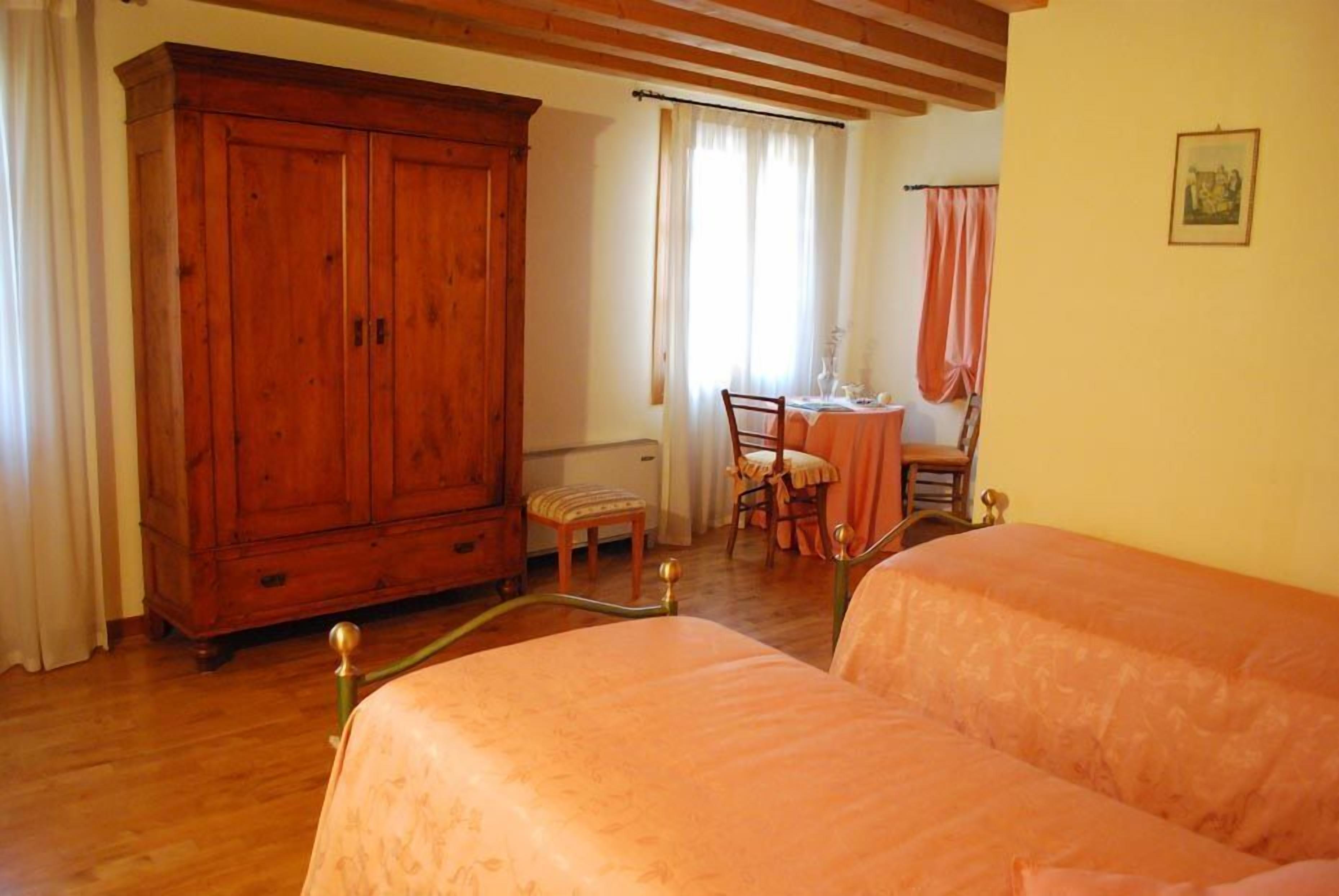 Une chambre avec deux lits, une armoire en bois, une table à manger avec des chaises et une fenêtre avec des rideaux.