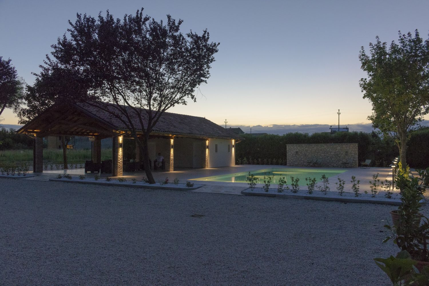 A covered outdoor area with a pool, surrounded by gravel and plants.
