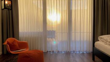 Una habitación con cama, una silla y un ventanal con cortinas ligeras.
