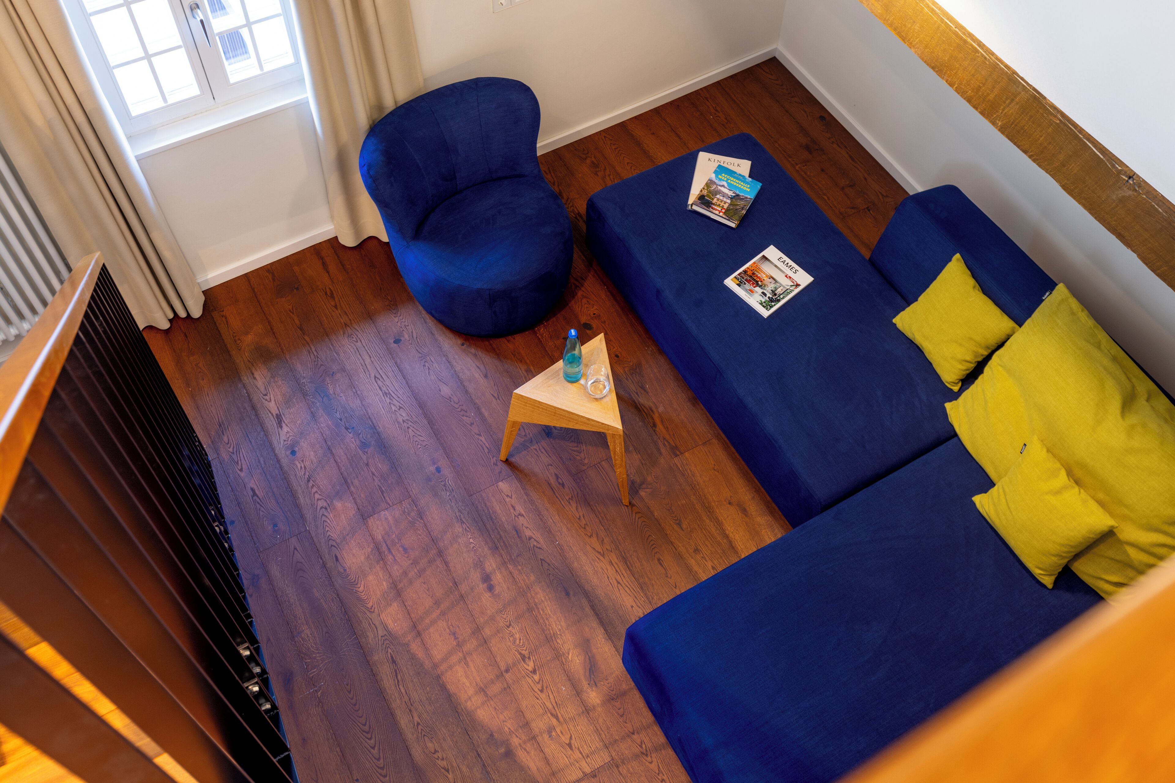 Une pièce avec un canapé bleu, un fauteuil bleu et une table d’appoint en bois sur laquelle se trouvent un magazine et une bouteille.