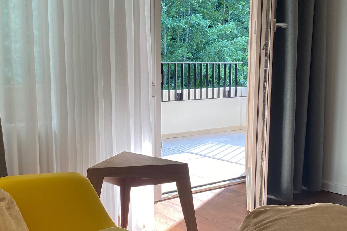 Une pièce avec un canapé jaune, une petite table en bois et une vue sur un balcon doté d’une balustrade.