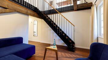 A modern living room with a wooden staircase, blue sofas, and a small wooden table.