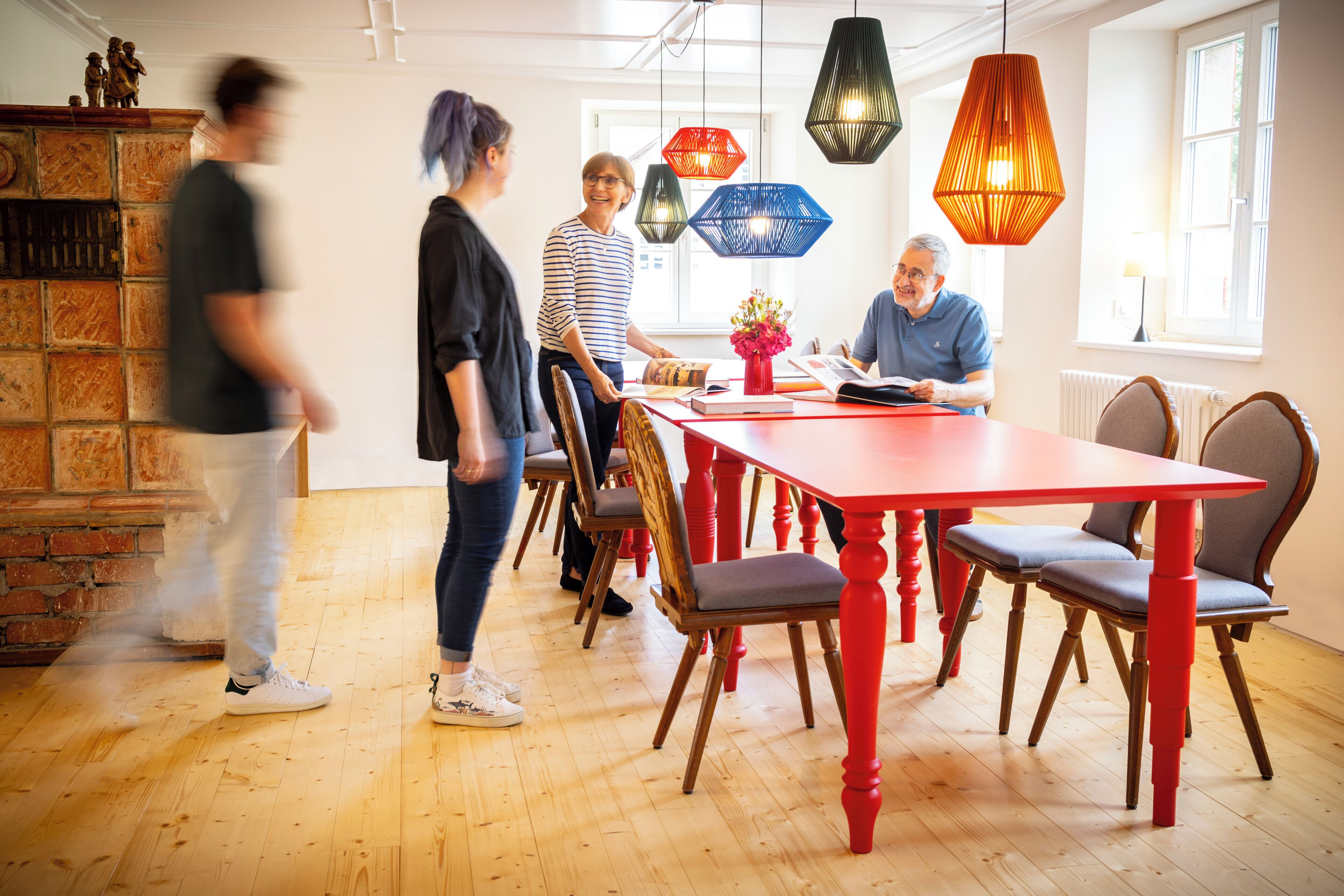 A modern dining area with a red table and wooden chairs, a brick wall, and pendant lights.