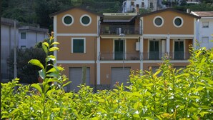 Un edificio de dos pisos con balcones, un letrero que dice "B&B MINIHOTEL IRIS" y un paisaje de colina de fondo.