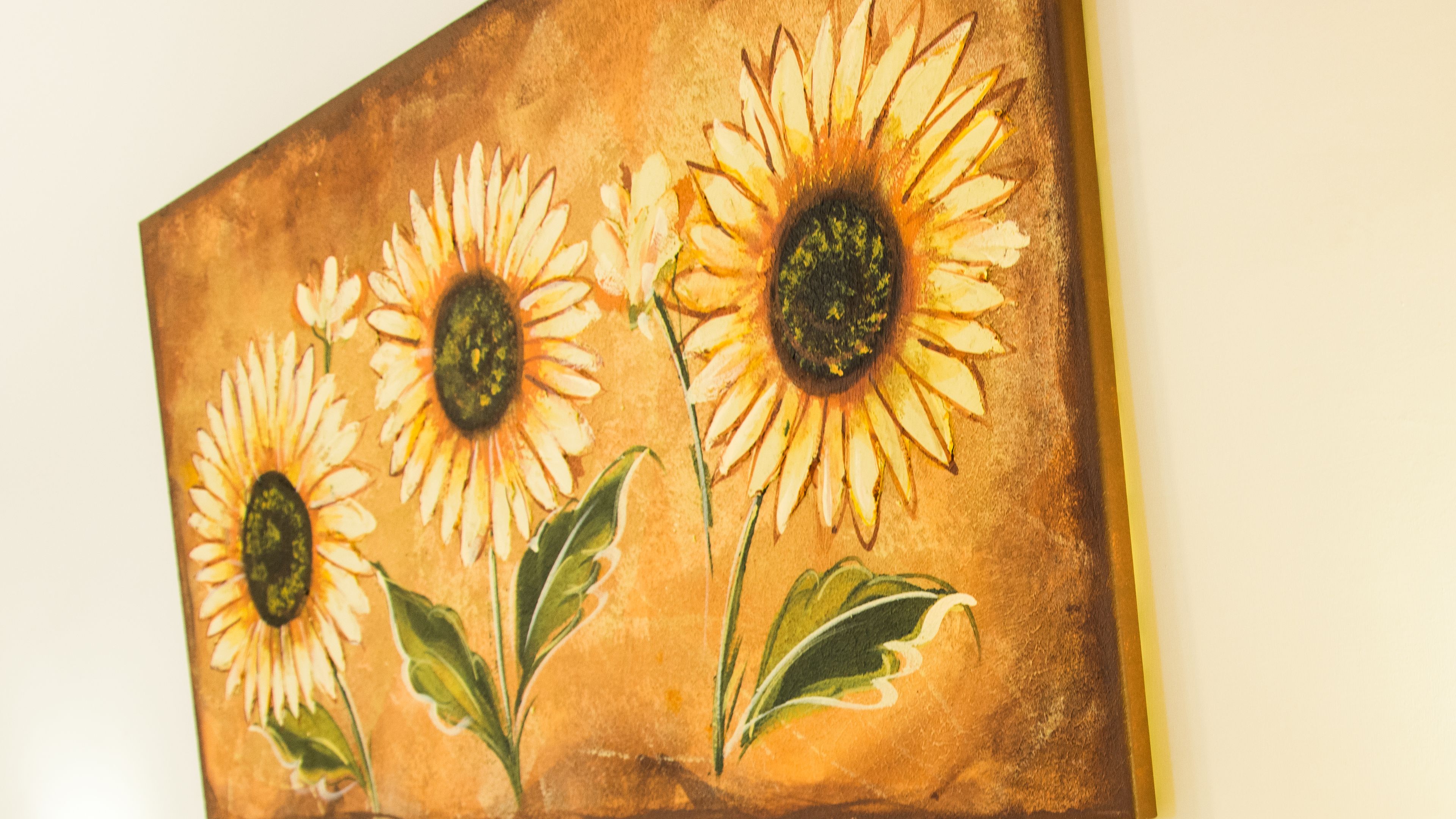 Pintura de tres girasoles con hojas verdes sobre un fondo marrón texturizado.