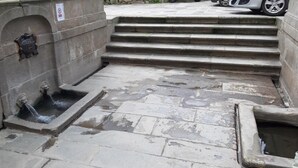 Una escalera de piedra que conduce a una fuente pequeña con una placa en la pared.