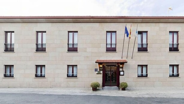 Un edificio con fachada simétrica, múltiples ventanas con barandillas oscuras y una entrada central con tejado de tejas rojas.