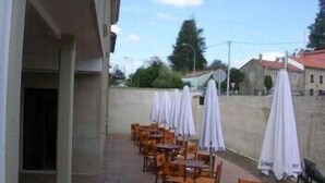 Un patio al aire libre con mesas y sillas de madera, cubierto por sombrillas blancas, y un muro de piedra al fondo.