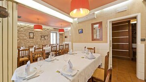 Un comedor con pared de piedra, sillas de madera y una mesa blanca lista para una comida.