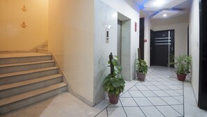 A hotel lobby with a staircase, potted plants, and a modern elevator.
