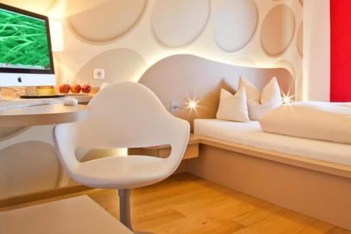 A modern bedroom with a curved headboard, a desk with a computer, and a white chair.