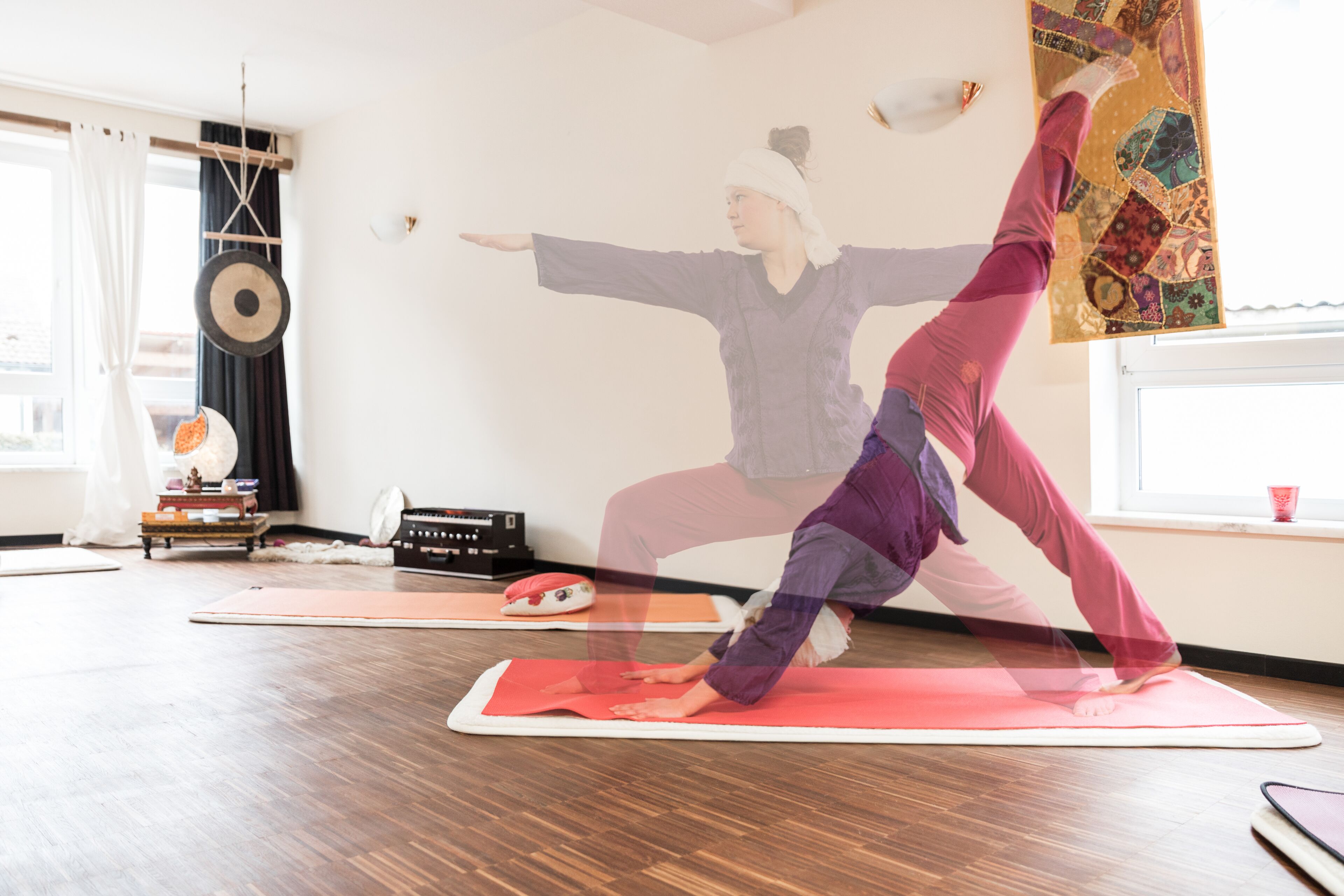 A yoga studio with wooden flooring, yoga mats, and a wall with a decorative tapestry.